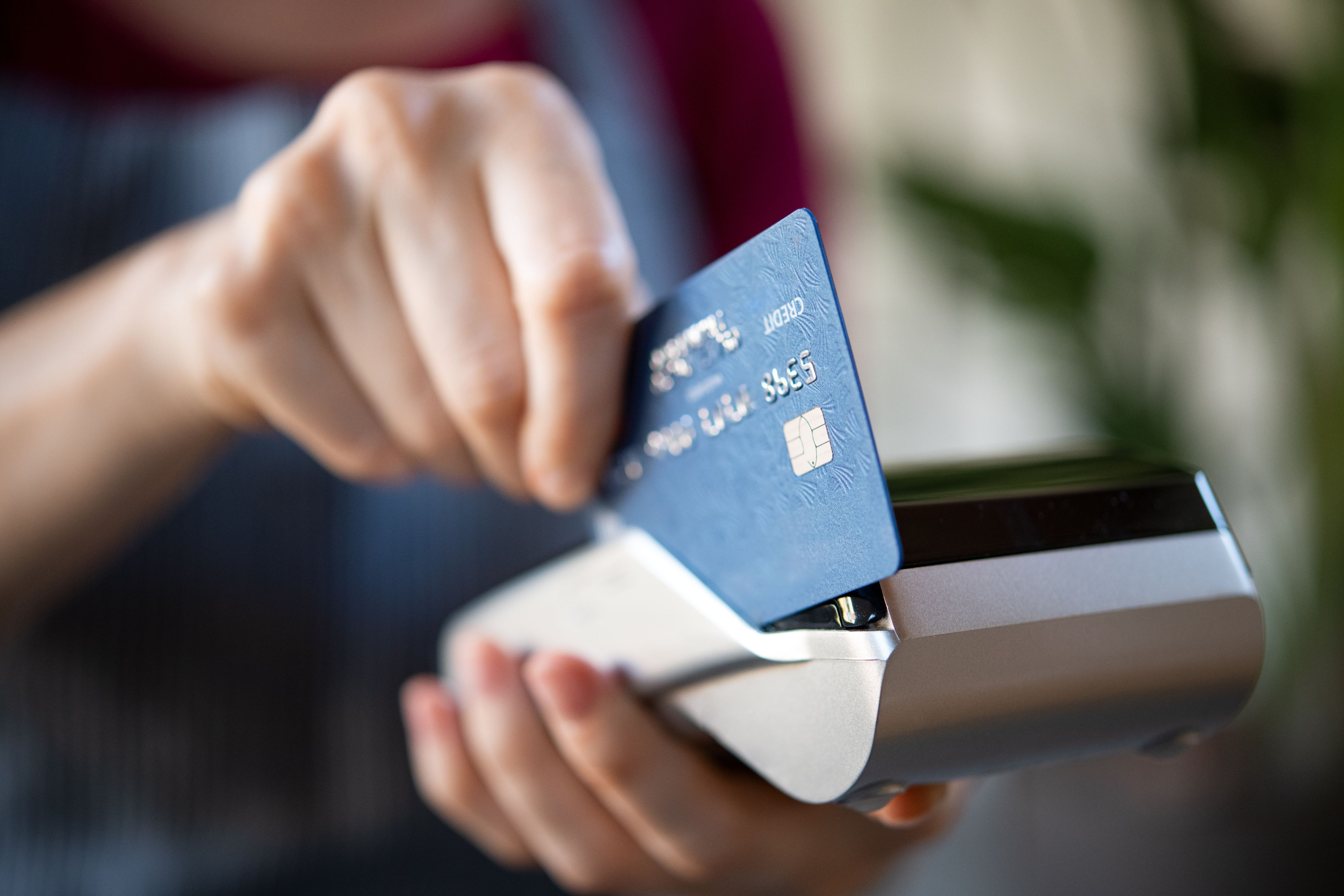 Close-up of a hand inserting a blue credit card into a payment terminal.